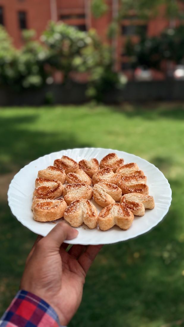 A hand holding a plate of sugar-topped palmiers on a lawn
