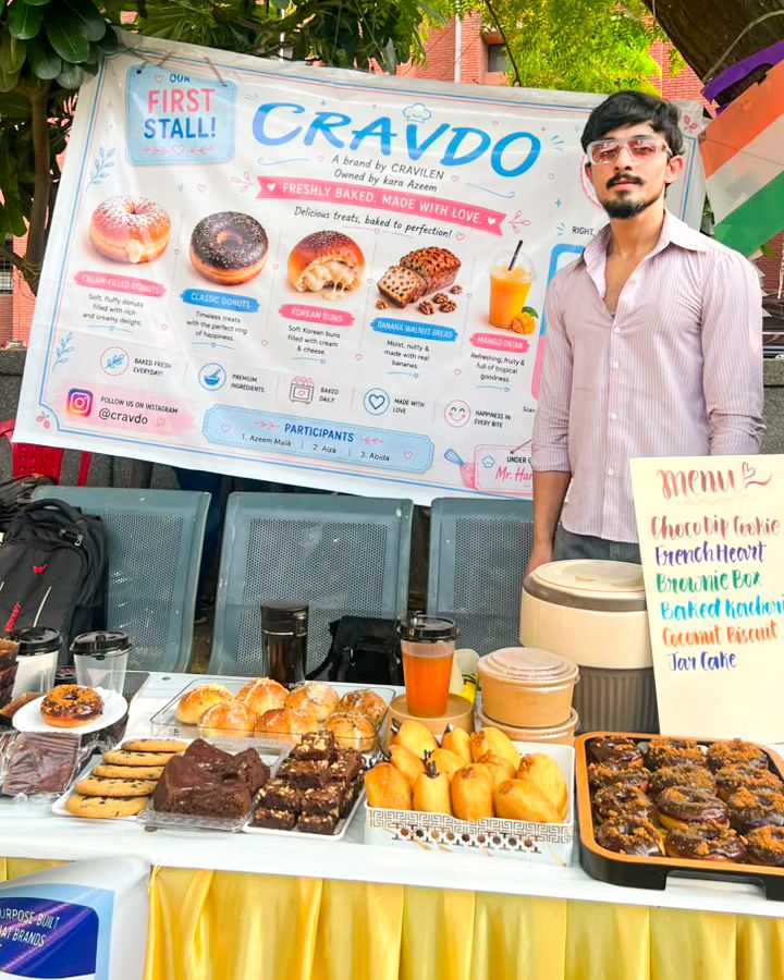 Azym Malik behind the first Cravdo stall, with the banner above trays of donuts, buns, cookies and brownies